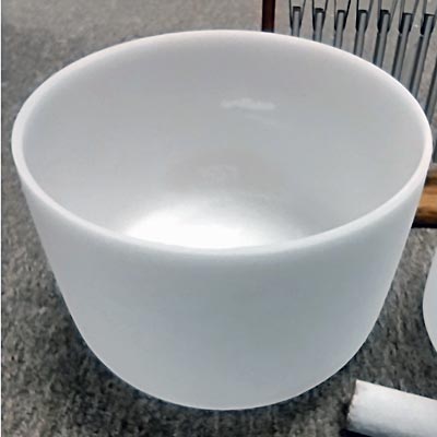 A frosted crystal singing bowl on a carpeted surface with a white mallet beside it, used for sound healing.
